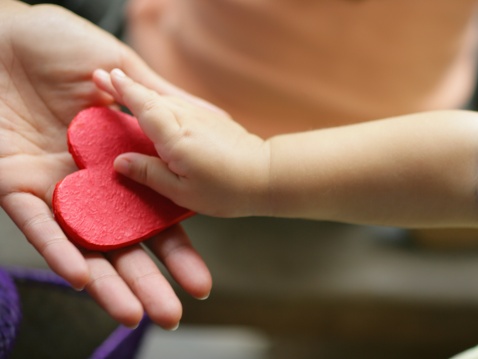 Close-up of a baby's hand giving valentine heart to another person